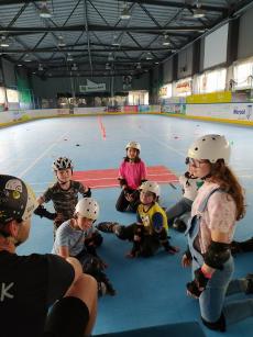 Powiększ zdjęcie: Grupa młodzieży słucha instruktora jazdy na rolkach na rolkowisku