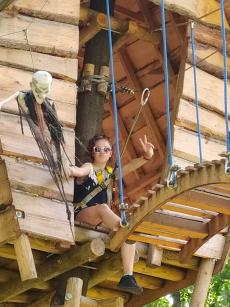 Powiększ zdjęcie: Nastolatka siedzi na podeście przed kolejnym odcinkiem trasy w parku linowym