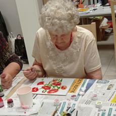 Powiększ zdjęcie: Seniorka z Dziennego Domu Senior+ maluje na szkle czerwone kwiaty