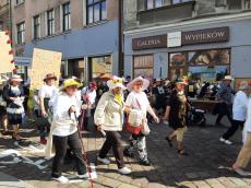 Powiększ zdjęcie: Seniorki w kapeluszach z kwiatami maszerują podczas Parady ulicą 11 Listopada