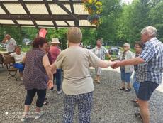 Powiększ zdjęcie: Seniorzy z Dziennego Domu Senior+ tanczą w kólku podczas spotkania plenerowego