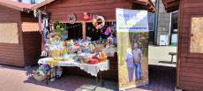 Powiększ zdjęcie: Stoisko Ośrodków Wsparcia dla Osób Starszych na Dniach Bielska-Białej. Drewniany domek wypełniony przedmiotami wykonanymi własnoręcznie przez seniorów.