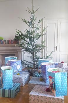 Powiększ zdjęcie: W pomieszczeniu stoi wysoka, udekorowana choinka otoczona świątecznymi paczkami z prezentami.