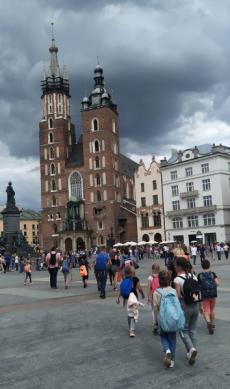 Powiększ zdjęcie: Wycieczka do Krakowa. Grupa dzieci z przewodnikiem na Rynku Głównym w Krakowie. W tle budynek Kościoła Mariackiego.