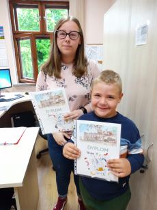 Powiększ zdjęcie: Zdjęcie przedstawia dwie osoby: chłopca i dziewczynkę, którzy z uśmiechem prezentują otrzymane dyplomy i nagrody.