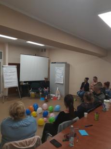 Powiększ zdjęcie: Zdjęcie przedstawia osoby uczestniczące w szkoleniu dla kandydatów na rodziny zastępcze niezawodowe. Wszystkie osoby siedzą w kręgu. W środku kręgu są porozrzucane balony.