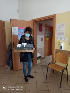 Powiększ zdjęcie:  Zdjęcie przedstawia Panią pełniącą funkcję rodziny zastępczej, która trzyma w rękach otrzymany w ramach projektu zestaw komputerowy.