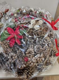 Powiększ zdjęcie: Zdjęcie przedstawia świąteczny stroik z szyszek ozdobiony kwiatem gwiazdą betlejemską.