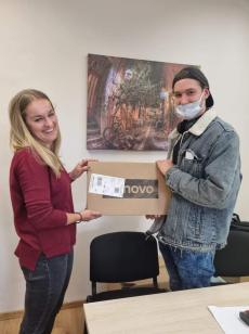 Powiększ zdjęcie: Zdjęcie przedstawia uśmiechniętą kobietę przekazującą nastolatkowi laptopa