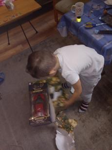 Powiększ zdjęcie: Zdjęcie przestawia pochylone dziecko, które rozpakowuje prezent, czerwony samochód.