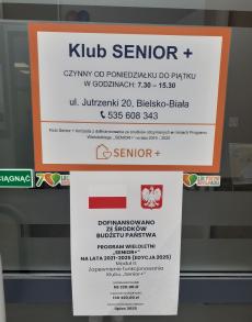 Powiększ zdjęcie: Drzwi wejściowe do Klubu Senior+ przy ul. Jutrzenki 20 w Bielsku-Białej z widocznym plakatem informacyjnym Programu Senior+ edycja 2025