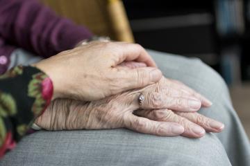 Dłoń młodej kobiety delikatnie gładzi splecione ze sobą ręce seniorki