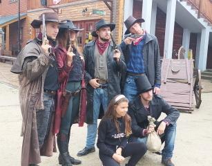 Miasteczko Twinpigs. Zdjęcie przedstawia dziewczynkę, która pozuje w towarzystwie czterech mężczyzn i jednej kobiety. Mężczyźni i kobieta są przebrani za kowboi, są animatorami w Miasteczku Twinpigs, czyli Amerykańskim Parku Rozrywki.