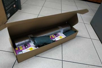 Zdjęcie pakietu energetycznego umieszczonego w pudełku z szarego kartonu leżacego na posadzce. W pakiecie znajdują się między innymi żarówki LED o ciepłobiałym świetle, z pseudowłóknami LED-owymi. Po zapaleniu daje to efekt świetlny tradycyjnej żarówki, przy pięciokrotnie mniejszej ilości zużytego prądu.