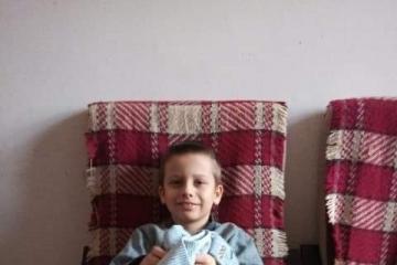 Zdjęcie przedstawia uśmiechniętego chłopca siedzącego na fotelu, który trzyma na kolanach prezent od Świętego Mikołaja